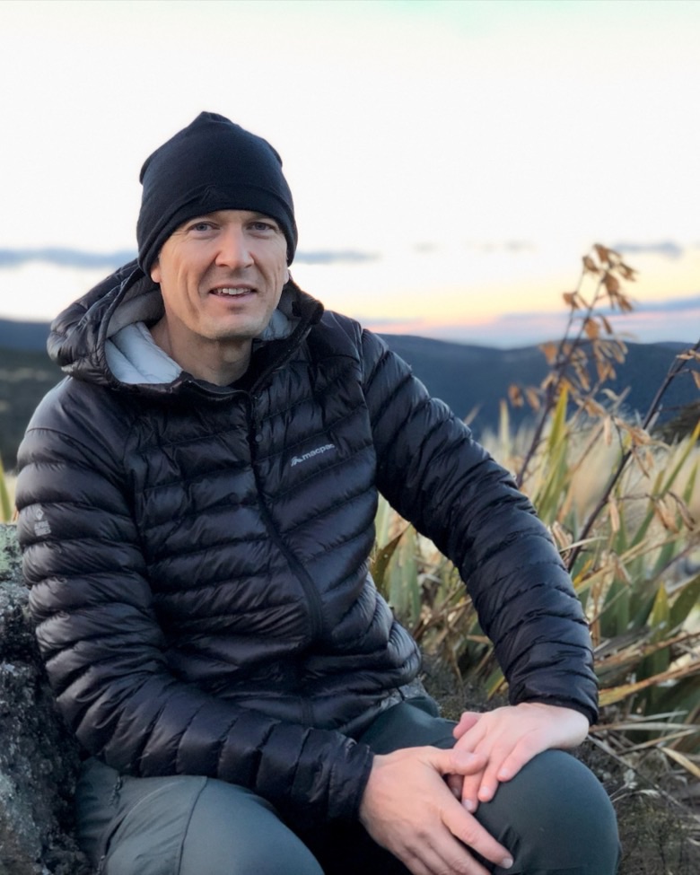 Scott, sitting against a rock in the New Zealand high country at dusk, flax behind him.